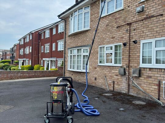 SkyVac Interceptor with a long pole reaching the top gutter of a three-storey block of flats
