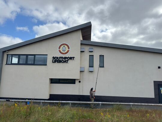 Cleaning the white render of a commercial building with a long pole from ground level