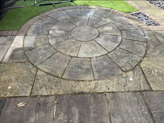 Before: stone circle patio with a brick border, next to artificial grass
